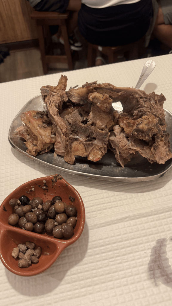A plate of cooked meat bones served on a metal platter, accompanied by a small bowl of various olives.
